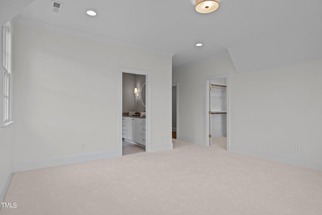 unfurnished bedroom with a closet, a spacious closet, light colored carpet, and ensuite bath