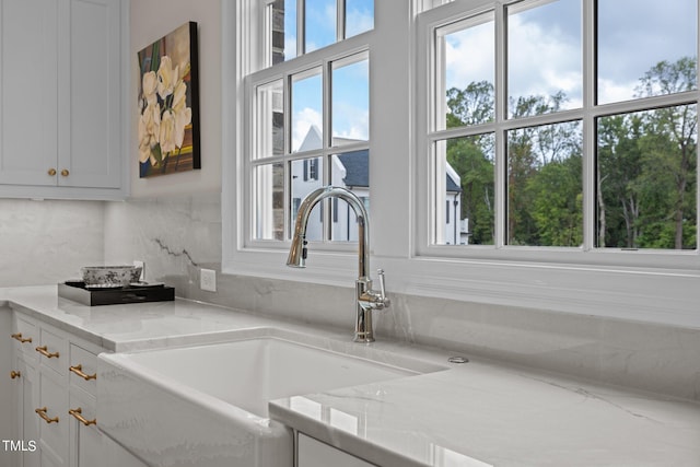 interior details featuring light stone countertops, backsplash, sink, and white cabinetry