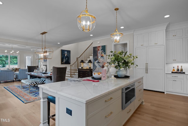 kitchen featuring pendant lighting, ornamental molding, a kitchen island, light hardwood / wood-style flooring, and white cabinetry