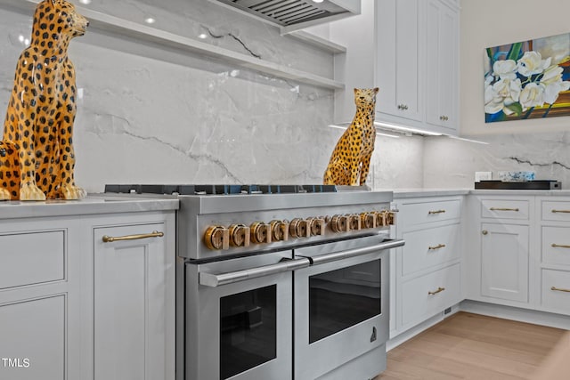 kitchen with tasteful backsplash, white cabinets, light stone countertops, light hardwood / wood-style flooring, and double oven range