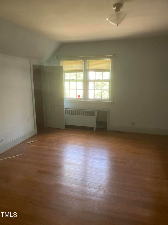 empty room featuring hardwood / wood-style flooring, radiator heating unit, and vaulted ceiling