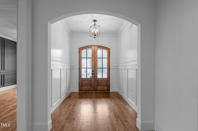 foyer featuring french doors, hardwood / wood-style flooring, crown molding, and a chandelier