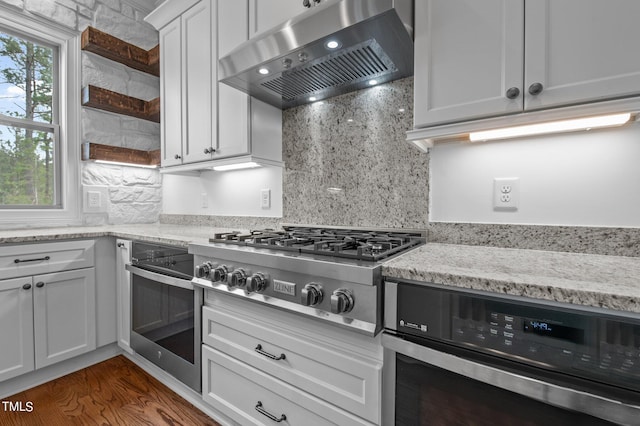 kitchen featuring appliances with stainless steel finishes, light stone counters, white cabinets, ventilation hood, and dark hardwood / wood-style floors