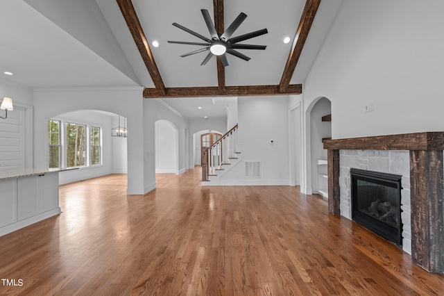 unfurnished living room featuring ceiling fan, beam ceiling, high vaulted ceiling, a fireplace, and hardwood / wood-style floors