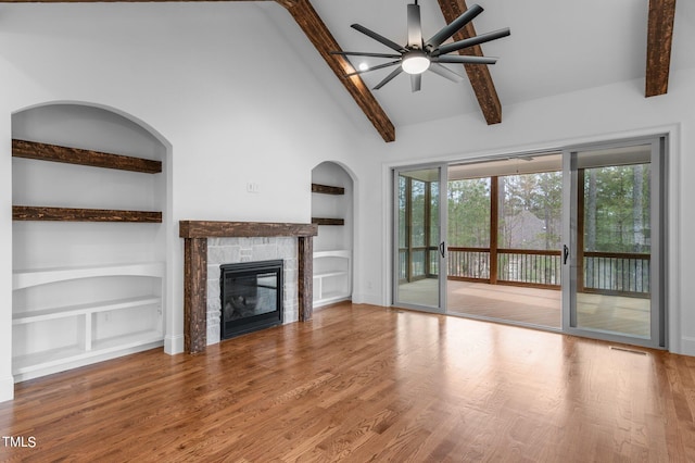 unfurnished living room featuring a stone fireplace, beamed ceiling, ceiling fan, built in features, and hardwood / wood-style flooring