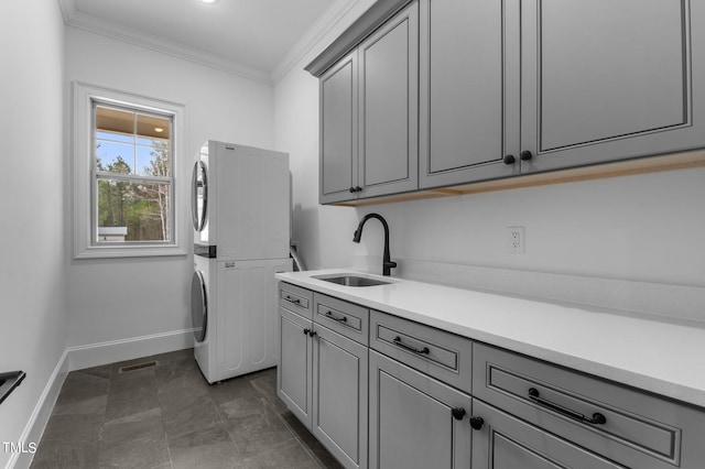 clothes washing area with cabinets, sink, ornamental molding, and stacked washing maching and dryer