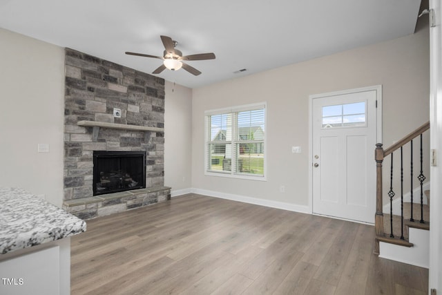 interior space featuring wood-type flooring, a stone fireplace, and ceiling fan