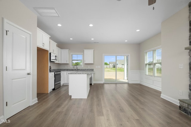 kitchen featuring appliances with stainless steel finishes, white cabinetry, a center island, and hardwood / wood-style floors