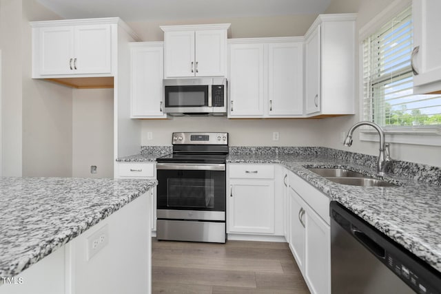 kitchen with white cabinetry, stainless steel appliances, light stone counters, hardwood / wood-style floors, and sink