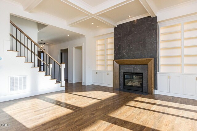 unfurnished living room featuring beamed ceiling, hardwood / wood-style floors, a high end fireplace, and built in shelves