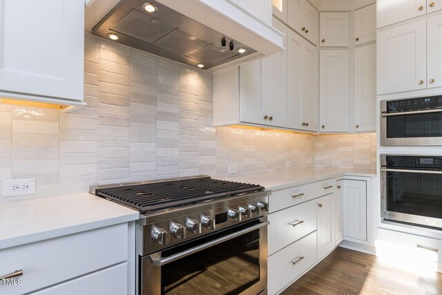 kitchen featuring white cabinetry, wood-type flooring, decorative backsplash, stainless steel appliances, and wall chimney exhaust hood