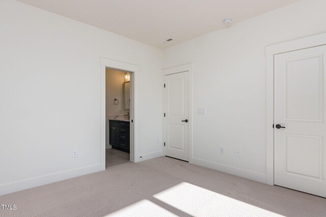 unfurnished bedroom featuring ensuite bath and light colored carpet