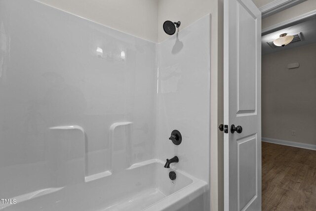 bathroom with washtub / shower combination and wood-type flooring