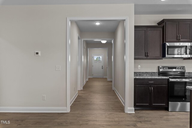 kitchen featuring dark brown cabinetry, light stone countertops, hardwood / wood-style flooring, and stainless steel appliances