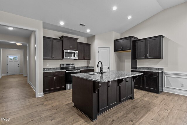 kitchen with lofted ceiling, an island with sink, stainless steel appliances, wood-type flooring, and sink