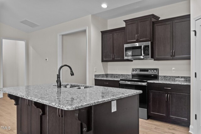 kitchen with appliances with stainless steel finishes, light hardwood / wood-style flooring, and a center island with sink