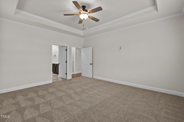 unfurnished bedroom with ensuite bath, ceiling fan, carpet floors, and a tray ceiling