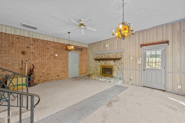 living room featuring carpet floors, ceiling fan with notable chandelier, brick wall, and a fireplace