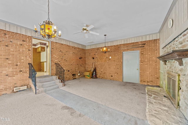 unfurnished living room with ceiling fan, light colored carpet, brick wall, a stone fireplace, and ornamental molding