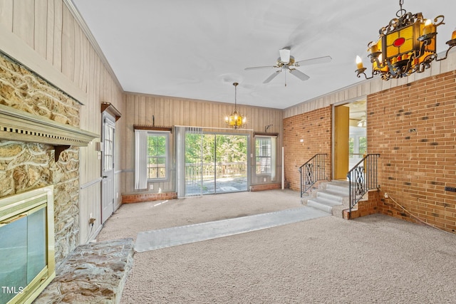 unfurnished living room with light carpet, ceiling fan with notable chandelier, wooden walls, and brick wall