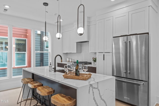 kitchen with a center island with sink, backsplash, white cabinets, high quality fridge, and a sink