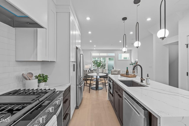 kitchen with appliances with stainless steel finishes, light wood-style floors, white cabinetry, and a sink