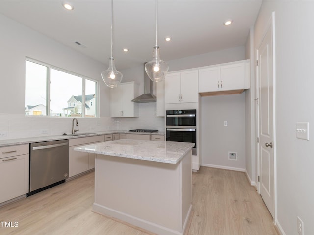 kitchen featuring wall chimney range hood, dishwasher, white cabinetry, a kitchen island, and decorative light fixtures