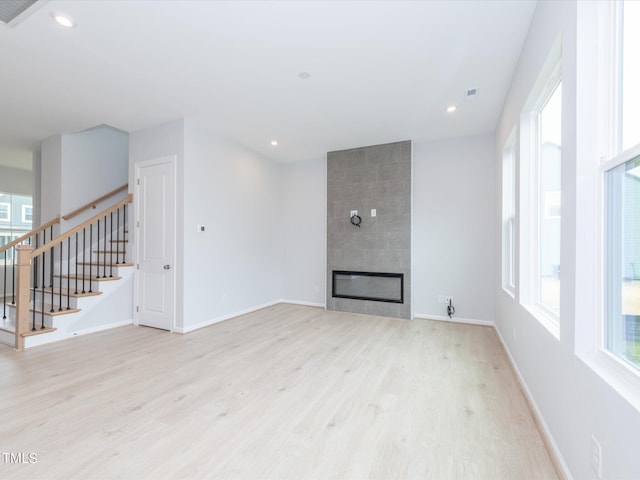 unfurnished living room with a healthy amount of sunlight, a large fireplace, and light hardwood / wood-style flooring