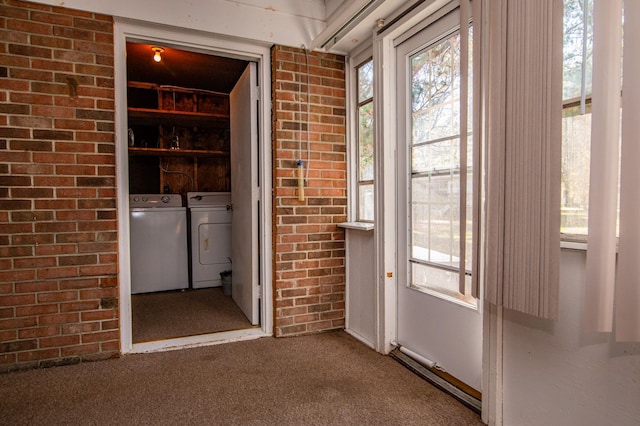 interior space featuring dark carpet, multiple windows, washer and dryer, and brick wall