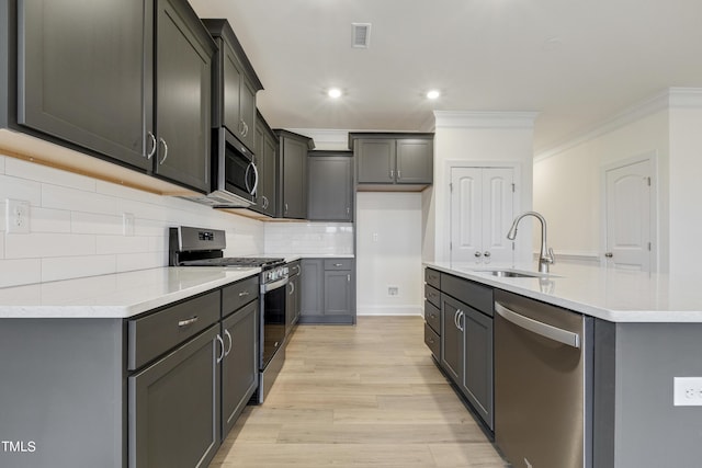 kitchen with a center island with sink, gray cabinetry, stainless steel appliances, light wood-type flooring, and ornamental molding