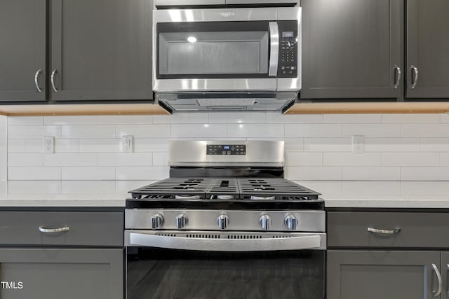 kitchen featuring light stone countertops, tasteful backsplash, gray cabinetry, and appliances with stainless steel finishes