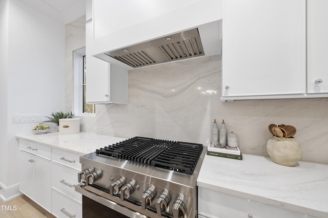 kitchen featuring white cabinetry, decorative backsplash, gas stove, light stone countertops, and wall chimney range hood