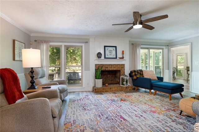 living room with wood-type flooring, ceiling fan, a brick fireplace, and crown molding