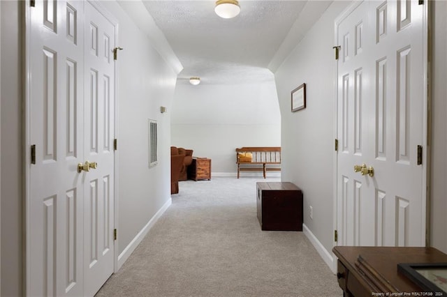 corridor with a textured ceiling and light carpet