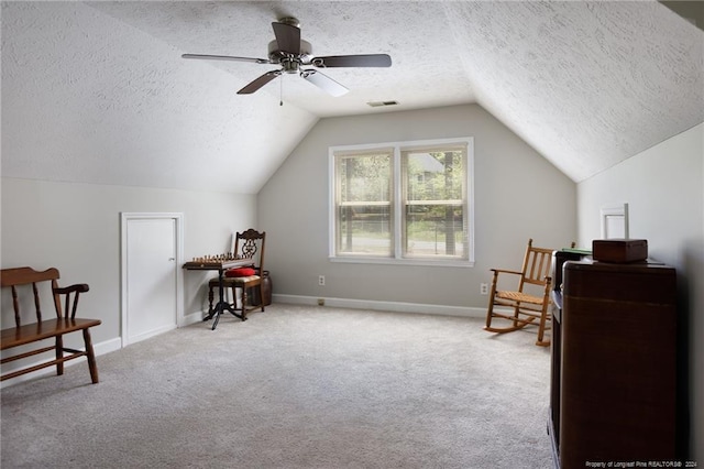 living area with carpet flooring, vaulted ceiling, ceiling fan, and a textured ceiling