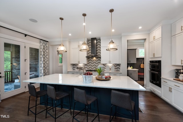 kitchen featuring white cabinets, wall chimney exhaust hood, a spacious island, and pendant lighting