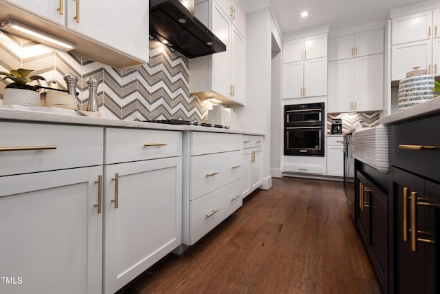 kitchen with white cabinets, black double oven, wall chimney range hood, decorative backsplash, and sink