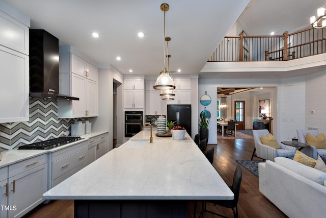 kitchen with decorative light fixtures, backsplash, wall chimney range hood, a spacious island, and black appliances