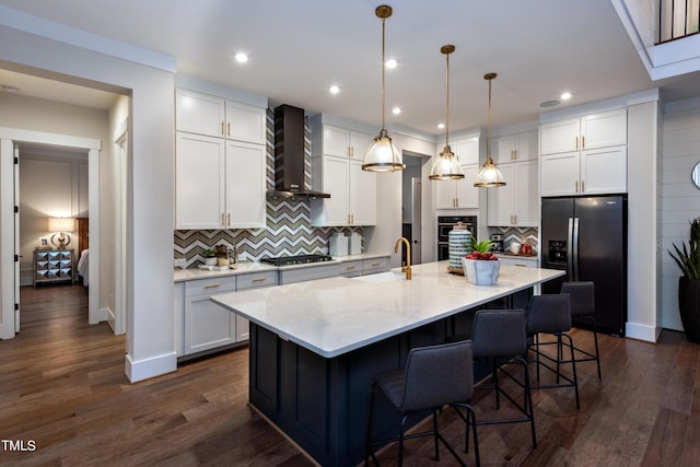 kitchen featuring a center island with sink, stainless steel appliances, hanging light fixtures, wall chimney range hood, and sink