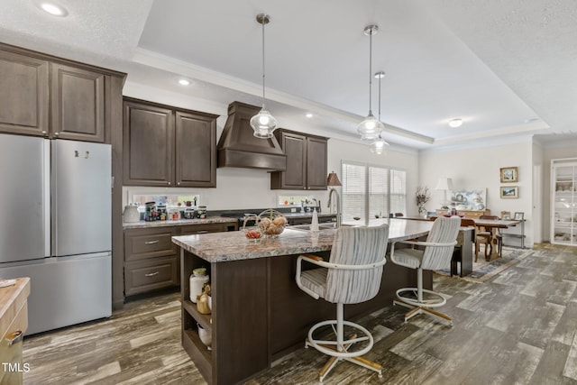 kitchen with a raised ceiling, custom exhaust hood, white fridge, and dark wood-type flooring