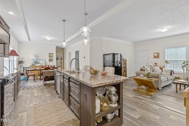 kitchen with light stone counters, light hardwood / wood-style flooring, sink, a center island with sink, and pendant lighting