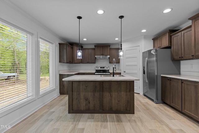 kitchen featuring dark brown cabinets, decorative light fixtures, appliances with stainless steel finishes, light hardwood / wood-style flooring, and an island with sink