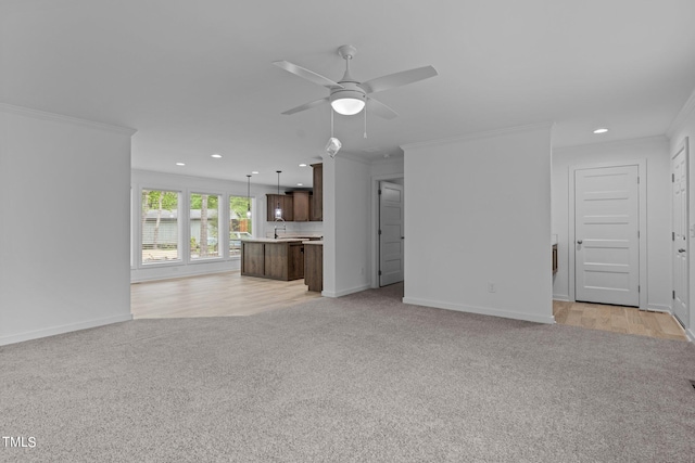 unfurnished living room featuring ornamental molding, light carpet, ceiling fan, and sink