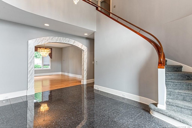 stairway with arched walkways, a chandelier, granite finish floor, recessed lighting, and baseboards