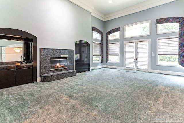 unfurnished living room with a towering ceiling, baseboards, carpet flooring, and a premium fireplace