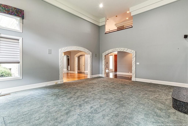 unfurnished living room featuring visible vents, arched walkways, baseboards, a high ceiling, and carpet flooring