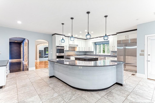 kitchen featuring decorative backsplash, a large island, white cabinetry, arched walkways, and appliances with stainless steel finishes