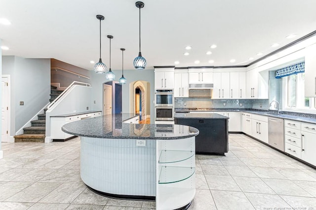 kitchen featuring a kitchen island, arched walkways, a sink, appliances with stainless steel finishes, and backsplash
