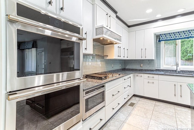 kitchen with appliances with stainless steel finishes, decorative backsplash, a sink, and premium range hood