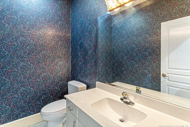 half bath featuring vanity, toilet, and wallpapered walls